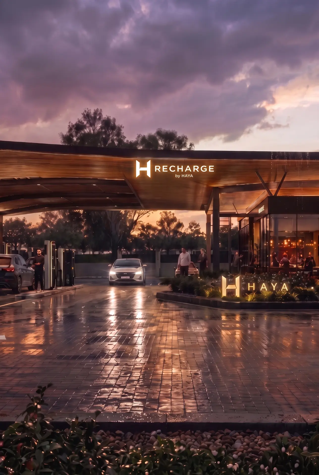 A RECHARGE by HAYA station at dusk with illuminated canopy signage, a car pulling in, and a welcoming lounge